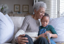 Estate Planning Strategies for Minor Children: Trump Accounts, 529 Plans, and Trusts A beautiful senior woman sits on a couch with her granddaughter as they read a story together while smiling.